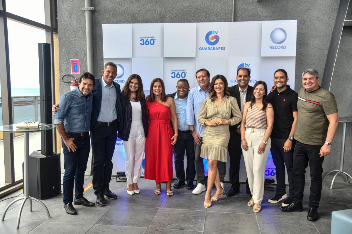 Apresentadores da TV Guararapes RECORD em frente ao telão com o logo das emissoras