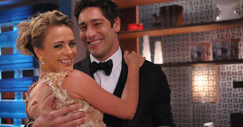 Juliana Silveira e Victor Pecoraro com roupa de gala e sorrindo em cena de Balacobaco