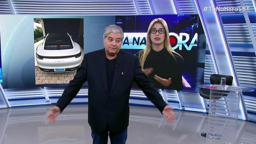 Datena abre os braços no estúdio do Tá na Hora visivelmente irritado com a repórter Nicole que aparece atrás dele no telão do SBT