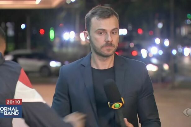 Igor Calian, com o microfone da Band nas mãos, com o ciclista passando e tentando puxar o celular