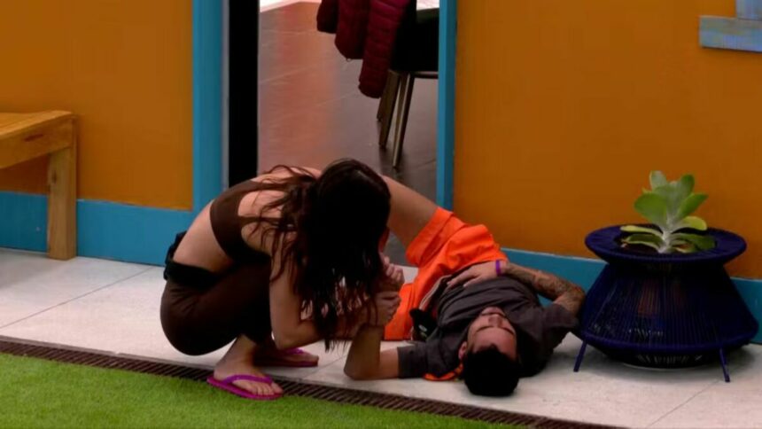 João Pedro caído no chão do BBB 25 e recebendo o apoio com as mãos de Vitória Strada
