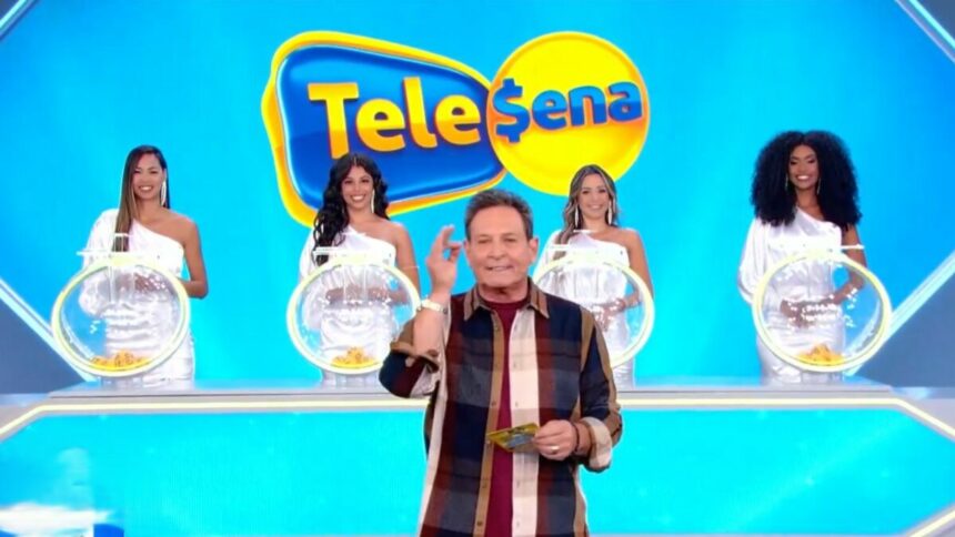 Luis Ricardo levanta o braço enquanto apresenta o sorteio da Tele Sena Semanal 48, o estúdio está azul