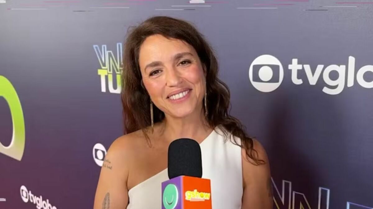 Manuela Dias em entrevista ao Gshow em frente a um banner de Vale Tudo
