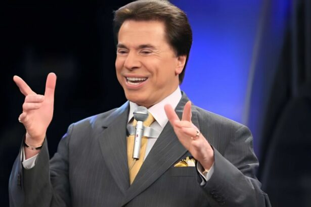 Silvio Santos com os braços levantados e o tradicional microfone colado na roupa. Ele está sorrindo