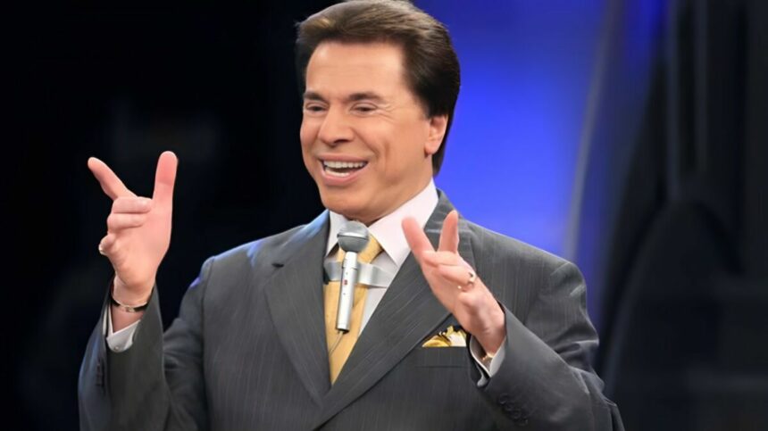 Silvio Santos com os braços levantados e o tradicional microfone colado na roupa. Ele está sorrindo