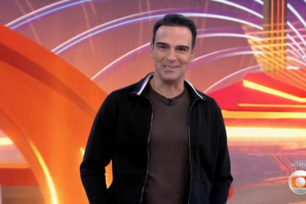 Tadeu Schmidt de camisa preta de botão e camisa cinza por dentro apresentando o BBB 25. Ele está sorrindo ao anunciar o BBB 26