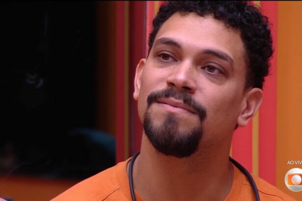 Vinicius, de camisa laranja, chora com discurso de Tadeu Schmidt antes da eliminação. Ele está sentado no sofá do BBB 25