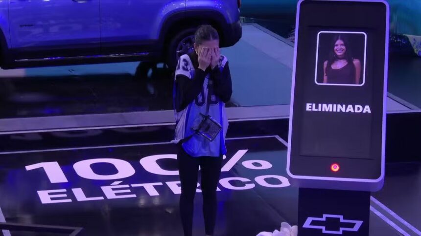 Vitória Strada chora ao ser eliminada da Prova do Finalista ao lado do carro da chevrolet. Ela coloca as mãos no rosto