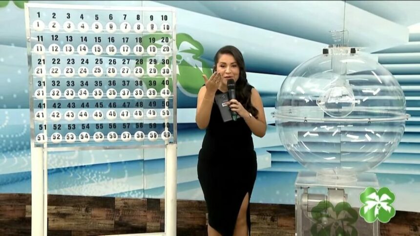 Apresentadora do Alagoas dá Sorte de vestido preto apresentando o painel com as bolas do sorteio do dia 27 de abril
