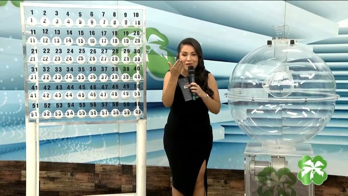 Apresentadora do Alagoas dá Sorte de vestido preto apresentando o painel com as bolas do sorteio do dia 27 de abril