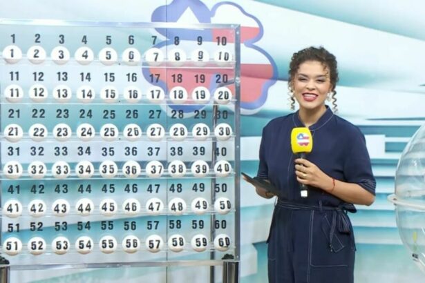 Apresentadora em pé segurando o microfone do Bahia dá Sorte em frente ao expositor com as bolas do sorteio