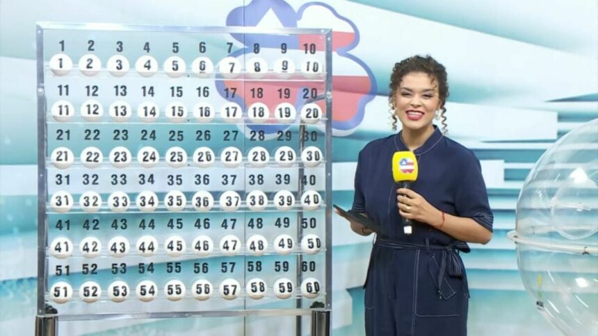 Apresentadora em pé segurando o microfone do Bahia dá Sorte em frente ao expositor com as bolas do sorteio