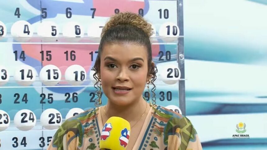 Apresentadora em pé segurando o microfone do Bahia dá Sorte em frente ao expositor com as bolas do sorteio no sorteio deste domingo 20 de abril