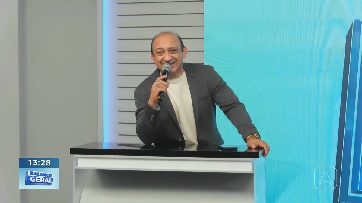 Beto Rêgo segura microfone de mão em cima da bancada do Balanço Geral PI