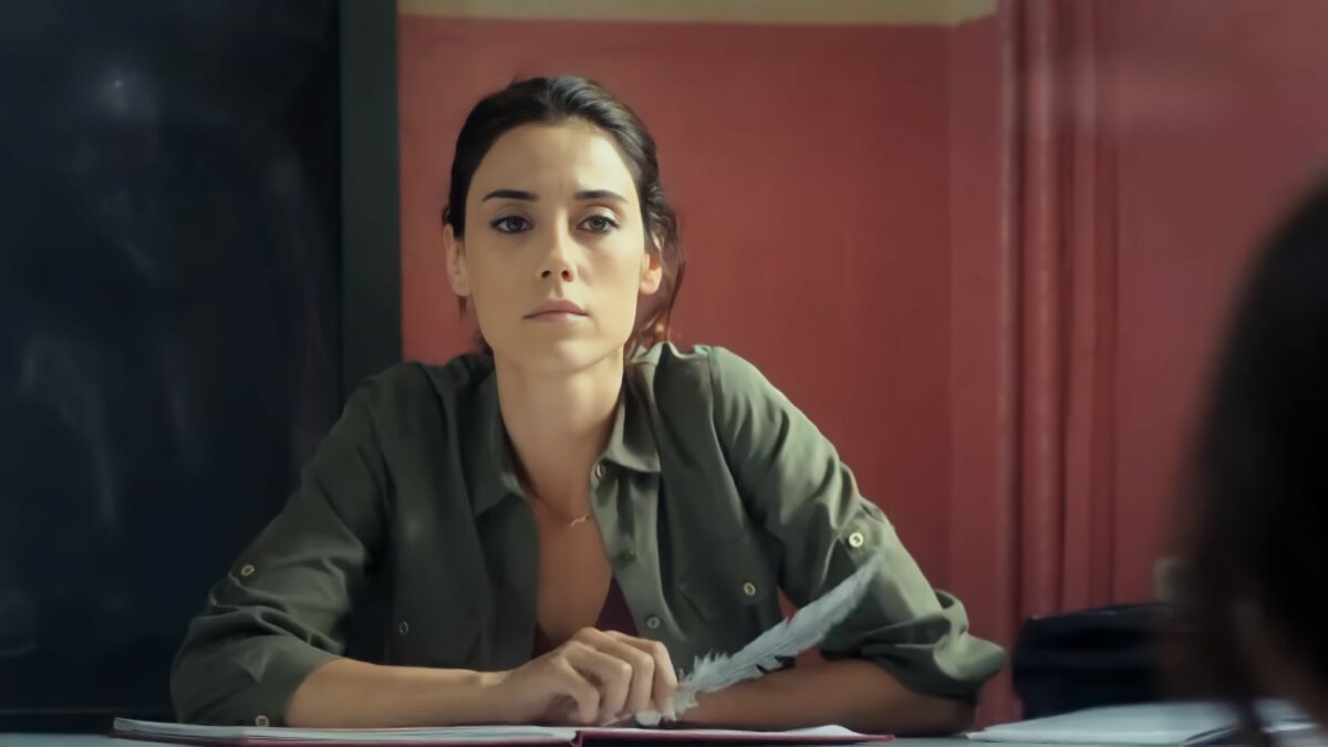 Cansu Dere, Zeynep Günes, sentada em uma mesa escolar, em cena dramática da novela turca Mãe, da RECORD. A personagem olha atentamente para a pequena Melek, que parece estar machucada