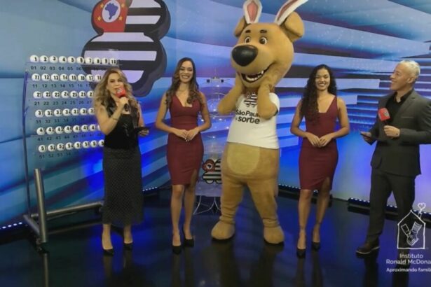 Mascote do São Paulo dá Sorte com orelhas de coelho ao lado das assistentes de palco e dos apresentadores no sorteio deste domingo 20 de abril