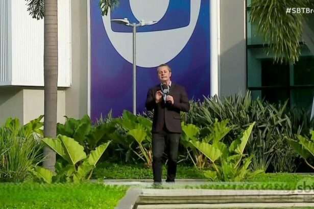 repórter Léo Sant’Anna gravando reportagem do SBT Brasil no jardim dos Estúdios Globo, em frente ao logo da TV Globo em azul