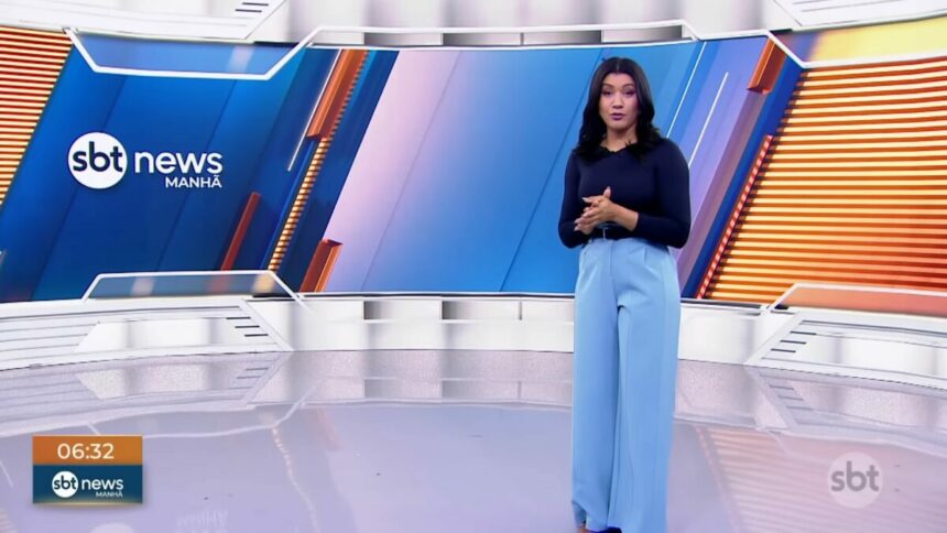 Dani Brandi em pé no centro no cenário do SBT News Manhã