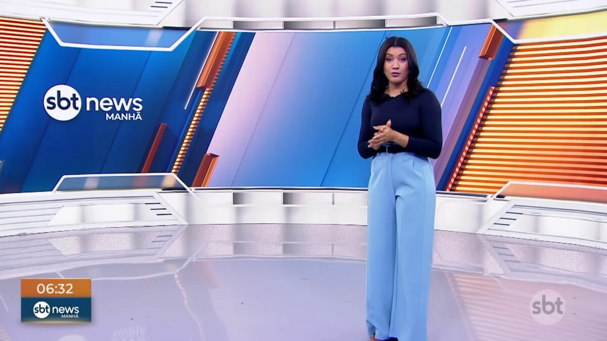 Dani Brandi em pé no centro no cenário do SBT News Manhã