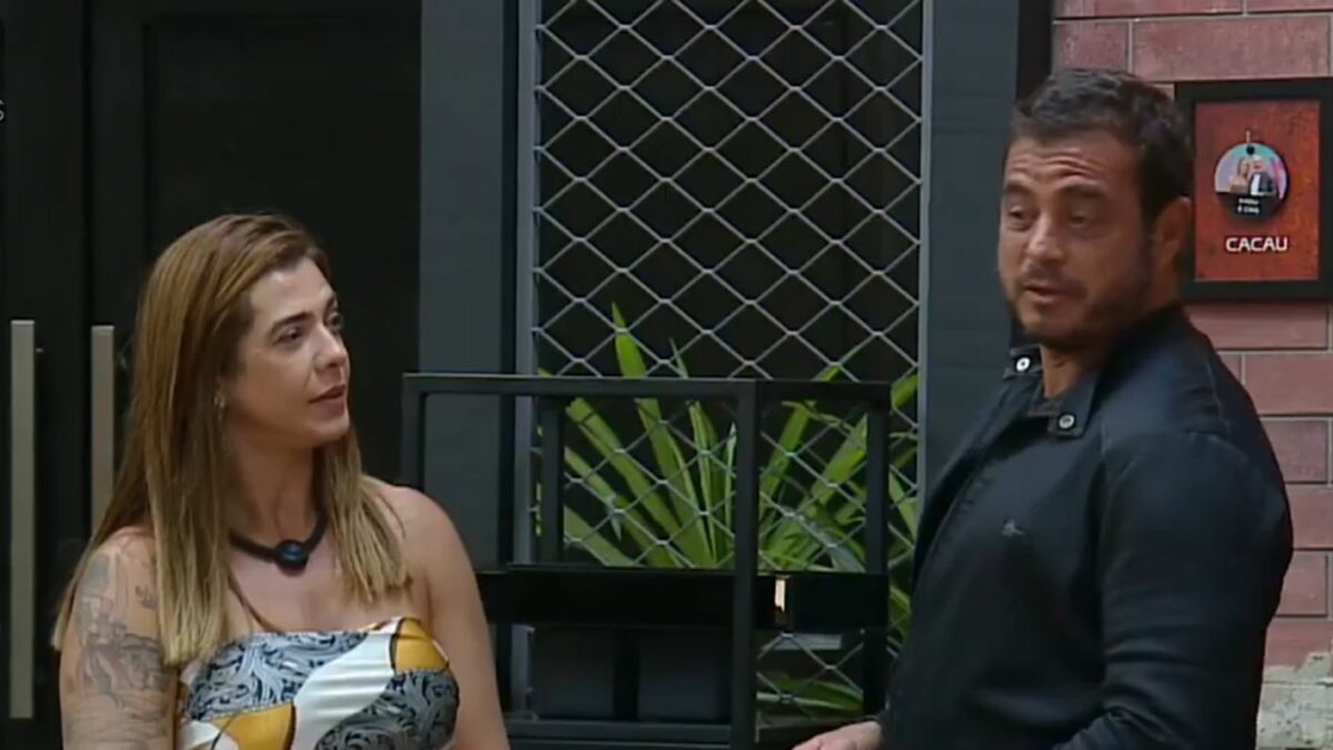 Adriana e Dhomini em frente ao quadro da divisão de quartos no Power Couple Brasil 7