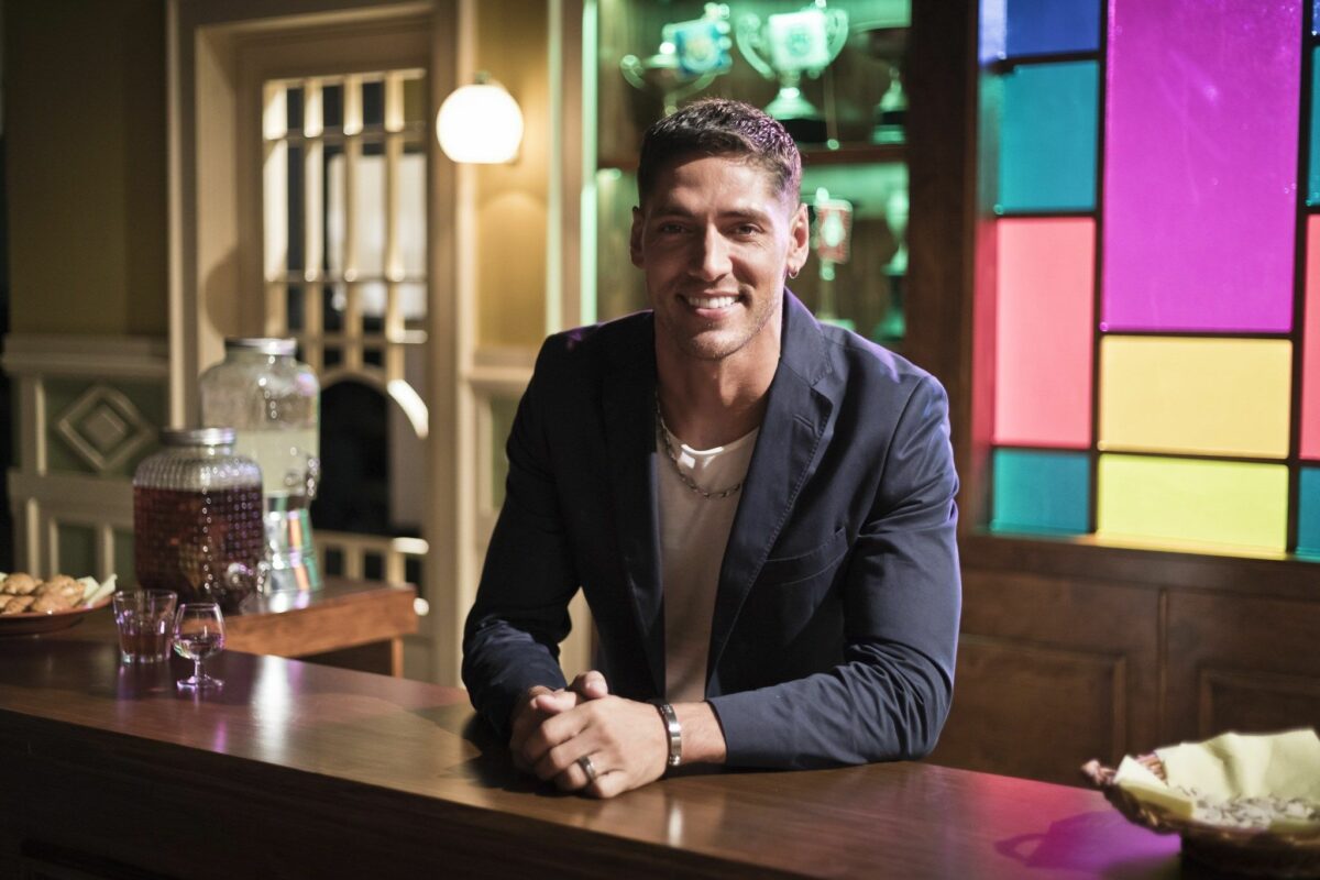Ângelo Rodrigues sorrindo em cima de um balcão em cena da novela Golpe de Sorte