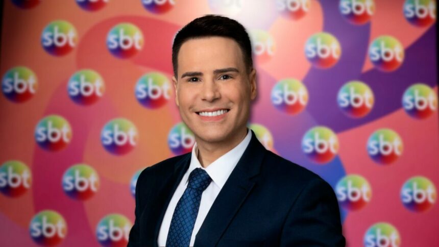 Luiz Bacci em frente ao painel com os logos do SBT