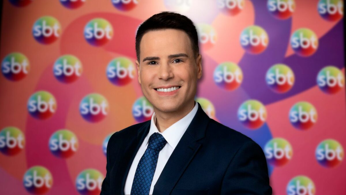 Luiz Bacci em frente ao painel com os logos do SBT