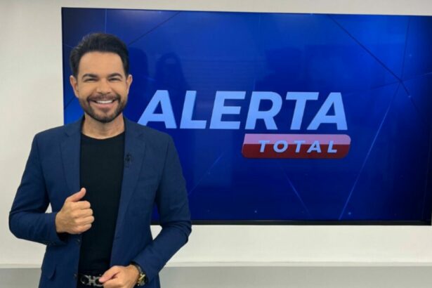 Apresentador Edinho Fernandes sorridente, em frente ao telão do Alerta Total