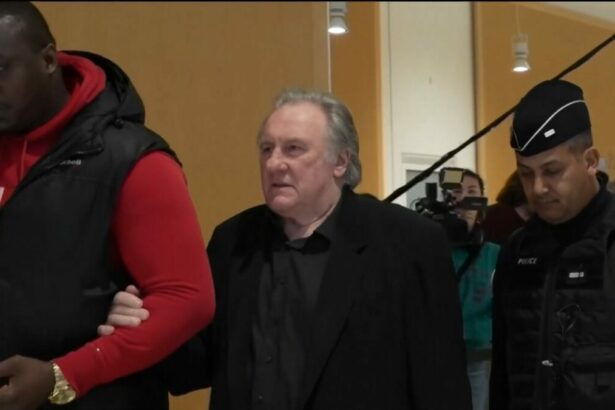 Gérard Depardieu caminha em um corredor acompanhados de policiais