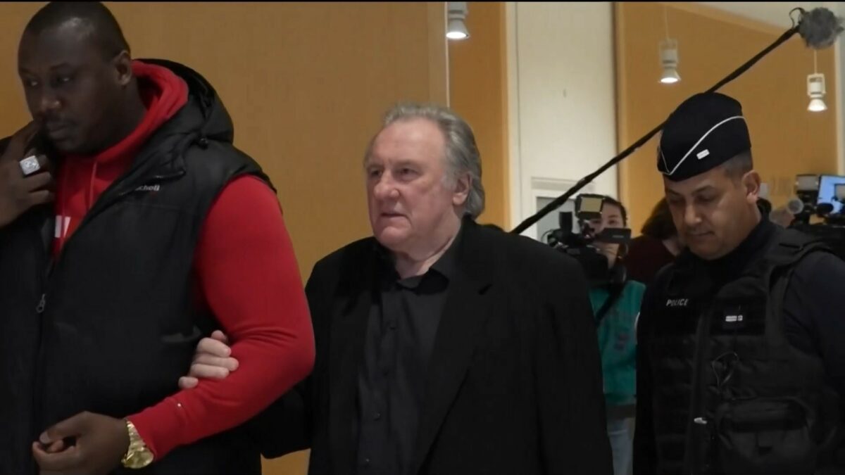 Gérard Depardieu caminha em um corredor acompanhados de policiais