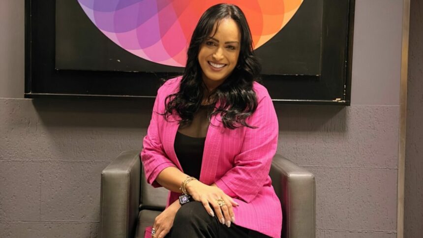 Lisa Gomes sentada em uma poltrona, em frente ao logo do SBT