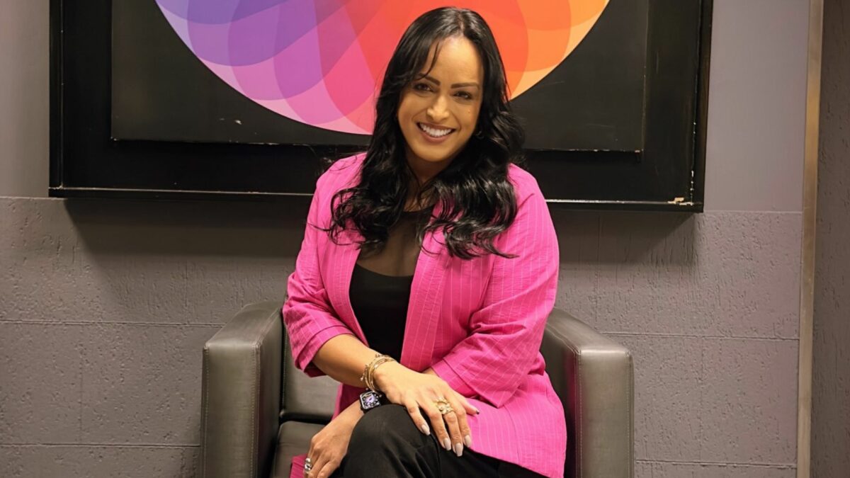 Lisa Gomes sentada em uma poltrona, em frente ao logo do SBT