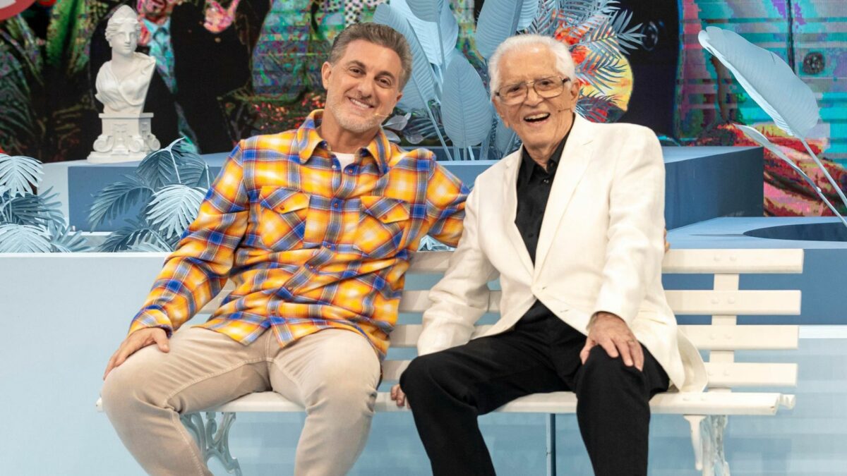 Luciano Huck e Carlos Alberto de Nóbrega sentados em um banco de praça no Domingão