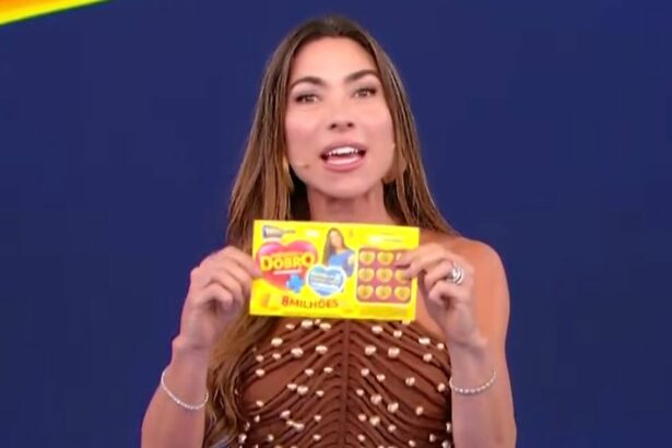Patricia Abravanel sorrindo e segurando o bilhete do quarto sorteio da Tele Sena de Mães 2025. Ela veste um vestido marrom.