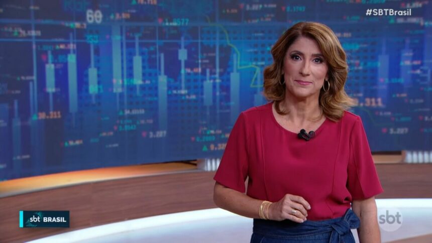 Simone Queiroz no cenário do SBT Brasil, vestida de blusa vermelha e saia azul