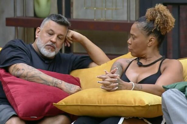 Silvia e André sentados no sofá do Power Couple