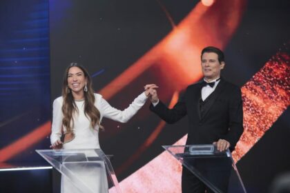 Patricia Abravanel de vestido branco, pega na mão de Celso Portiolli e levanta, na gravação do Troféu Imprensa. Os dois estão sorridentes e Celso veste terno preto com gravata borboleta