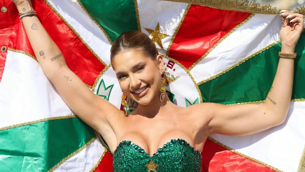 Virginia Fonseca sorrindo e segurando a bandeira Grande Rio