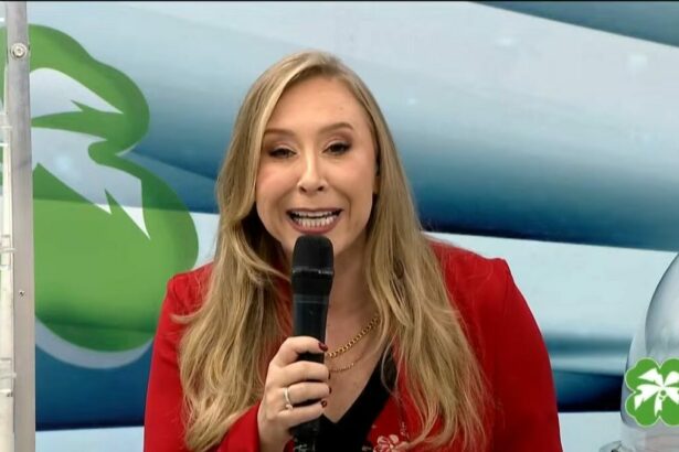 Apresentadora do Alagoas da Sorte em frente ao painel com as bolas do sorteio de 11 de maio. Ela segura um microfone preto