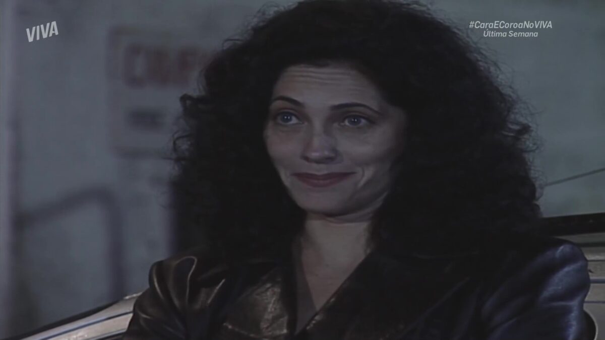 Fernanda sorrindo em frente ao local do cativeiro em cena de Cara e Coroa