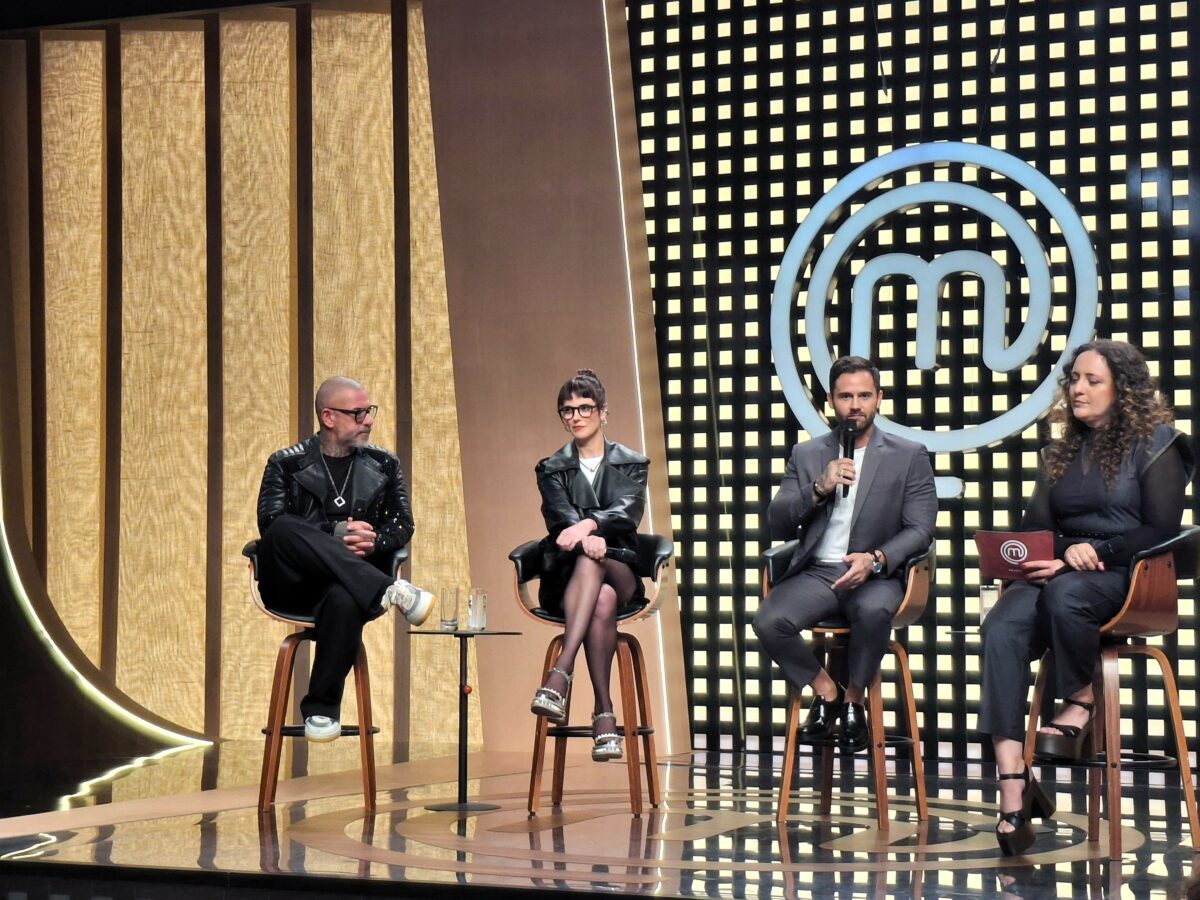 Henrique Fogaça, Helena Rizzo, Diego Lozano e a diretora Marisa Mestiço sentados em banquinhos no palco do novo cenário do MasterChef Brasil 2025