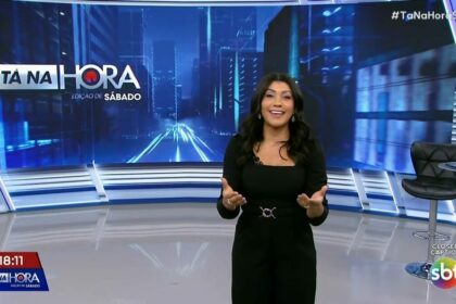 Dani Brandi de vestido preto e sorridente no cenário do SBT