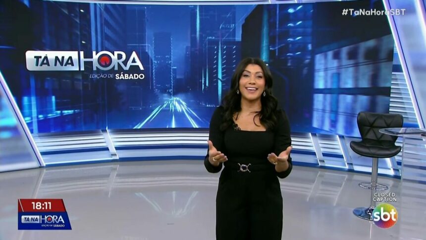 Dani Brandi de vestido preto e sorridente no cenário do SBT