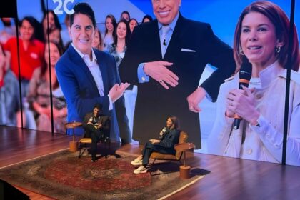 Cesar Filho sentado ao lado de Daniela Beyruti. Eles estão em frente a um telão gigante que trás imagens dos dois e de Silvio Santos no Rio2C