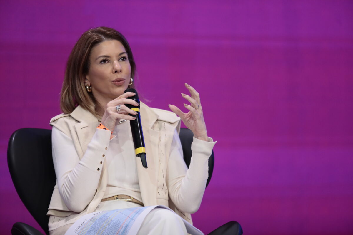 Daniela Beyruti segura um microfone na coletiva de imprensa do SBT, sentada em uma cadeira