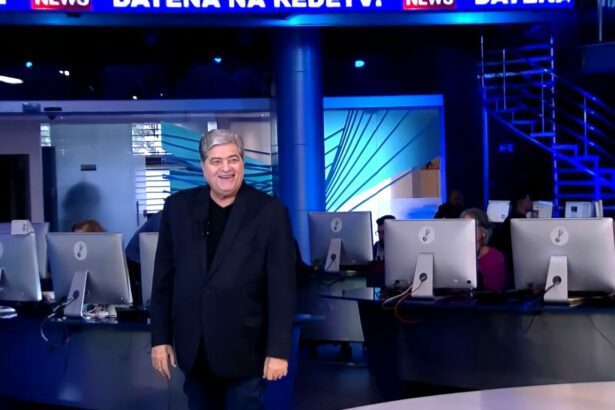 Datena em pé na redação da RedeTV!. Ele está sorridente