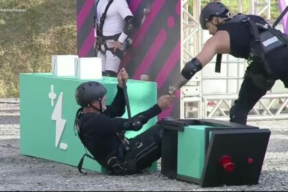 Diego segura na mão de Kadu Moliterno que está caído no chão de terra da Prova dos Homens do Power Couple Brasil 7