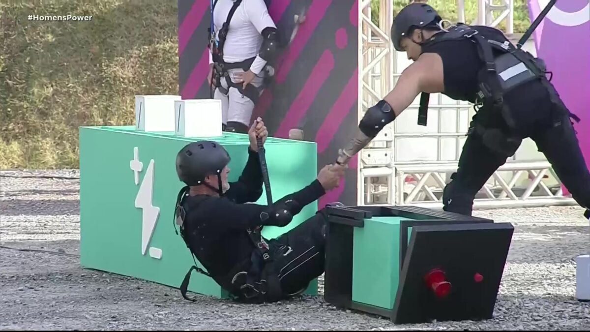 Diego segura na mão de Kadu Moliterno que está caído no chão de terra da Prova dos Homens do Power Couple Brasil 7