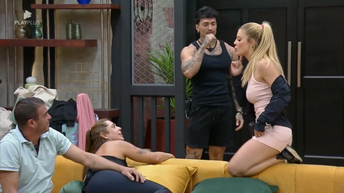 Giovanna senta no sofá da sala enquanto Diego entra no ambiente e comenta a disputa