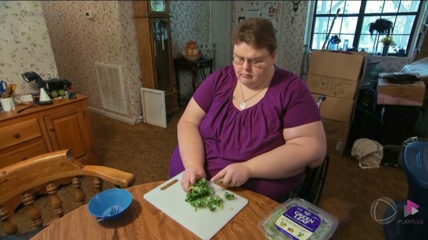 Holly, de blusa vinho, sentada em uma cadeira de rodas cortando alfaces em cena do Quilos Mortais